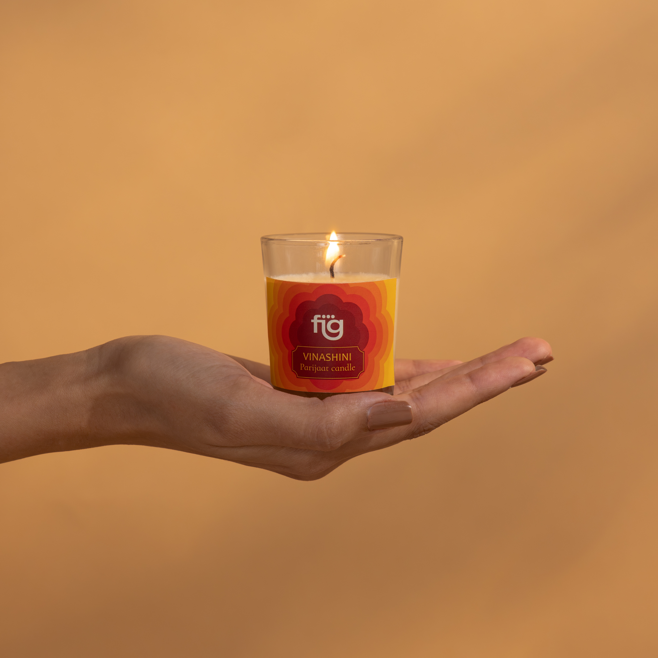 Hand holding a lit candle with a visible brand label against an orange background
