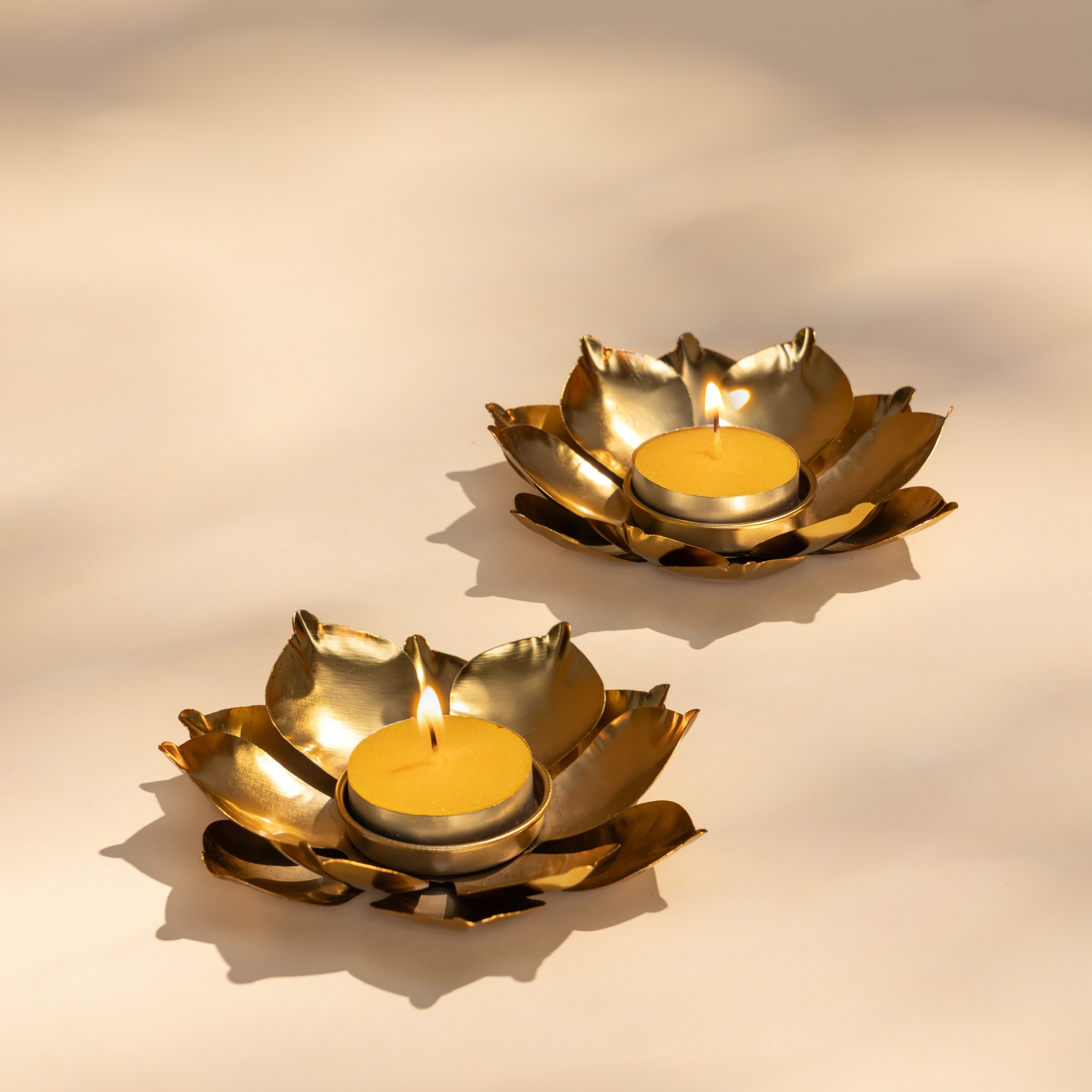 Two gold lotus-shaped candle holders for Diwali with lit candles