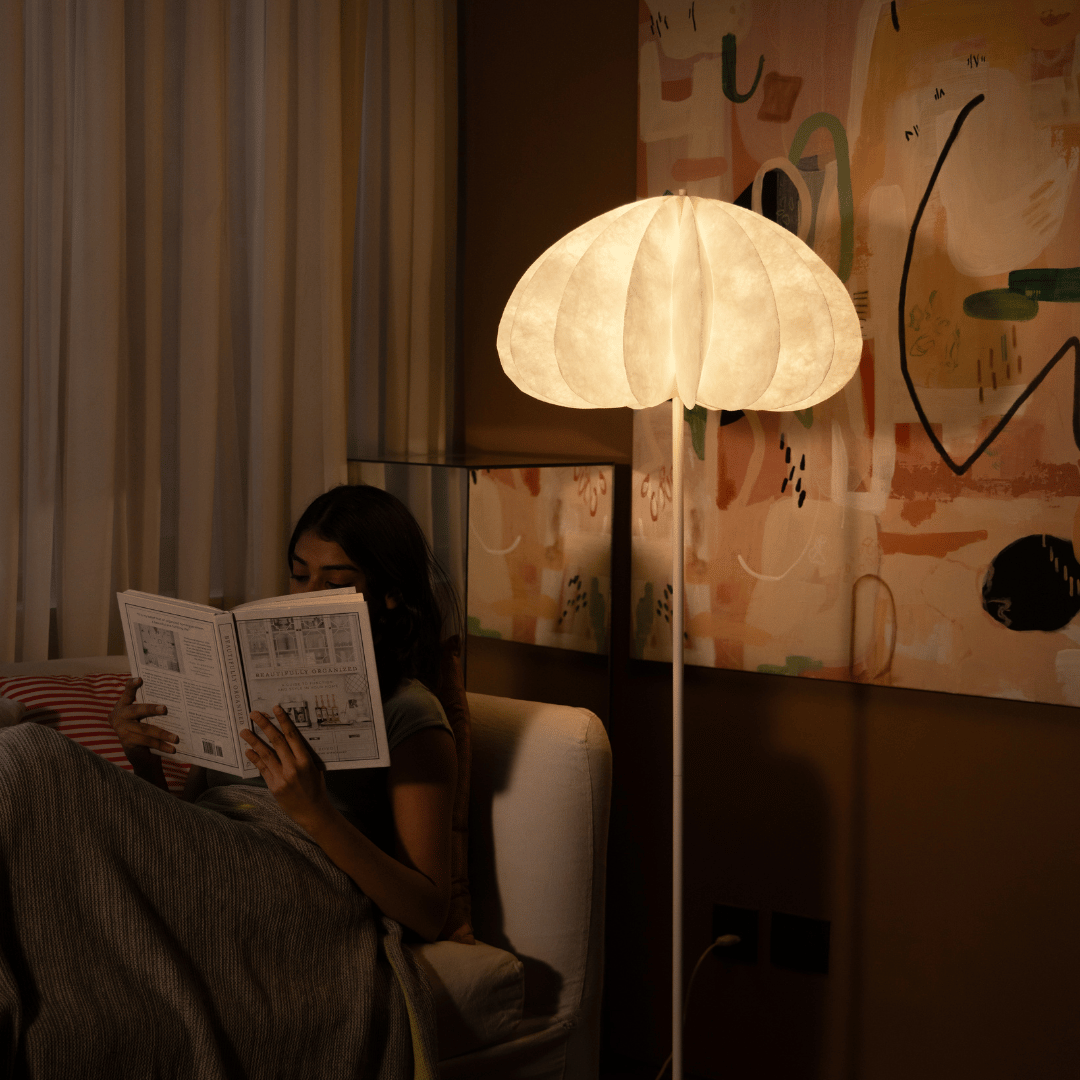 Person reading a newspaper in a dimly lit room with a large Daisy floor lamp.