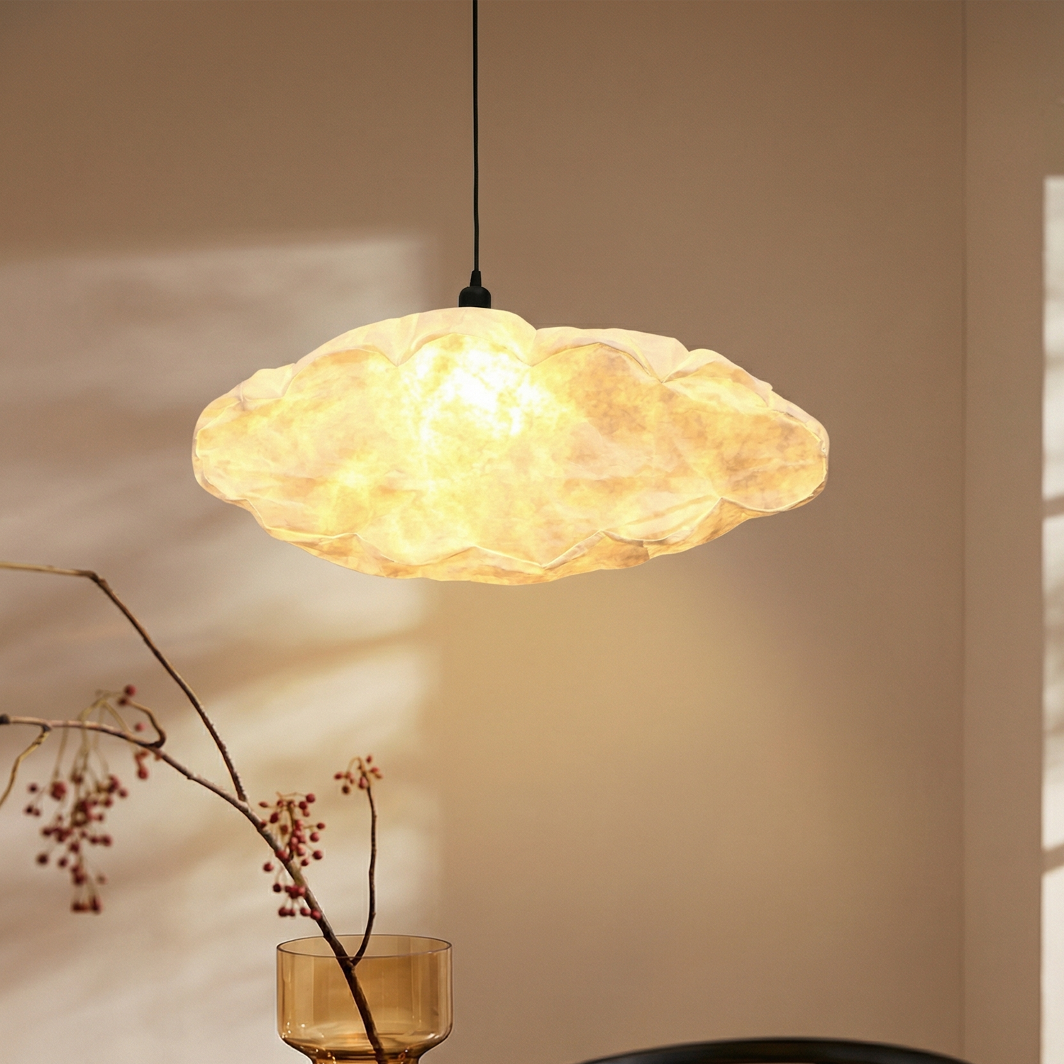 Decorative pendant light hanging above a table with a vase and branches.