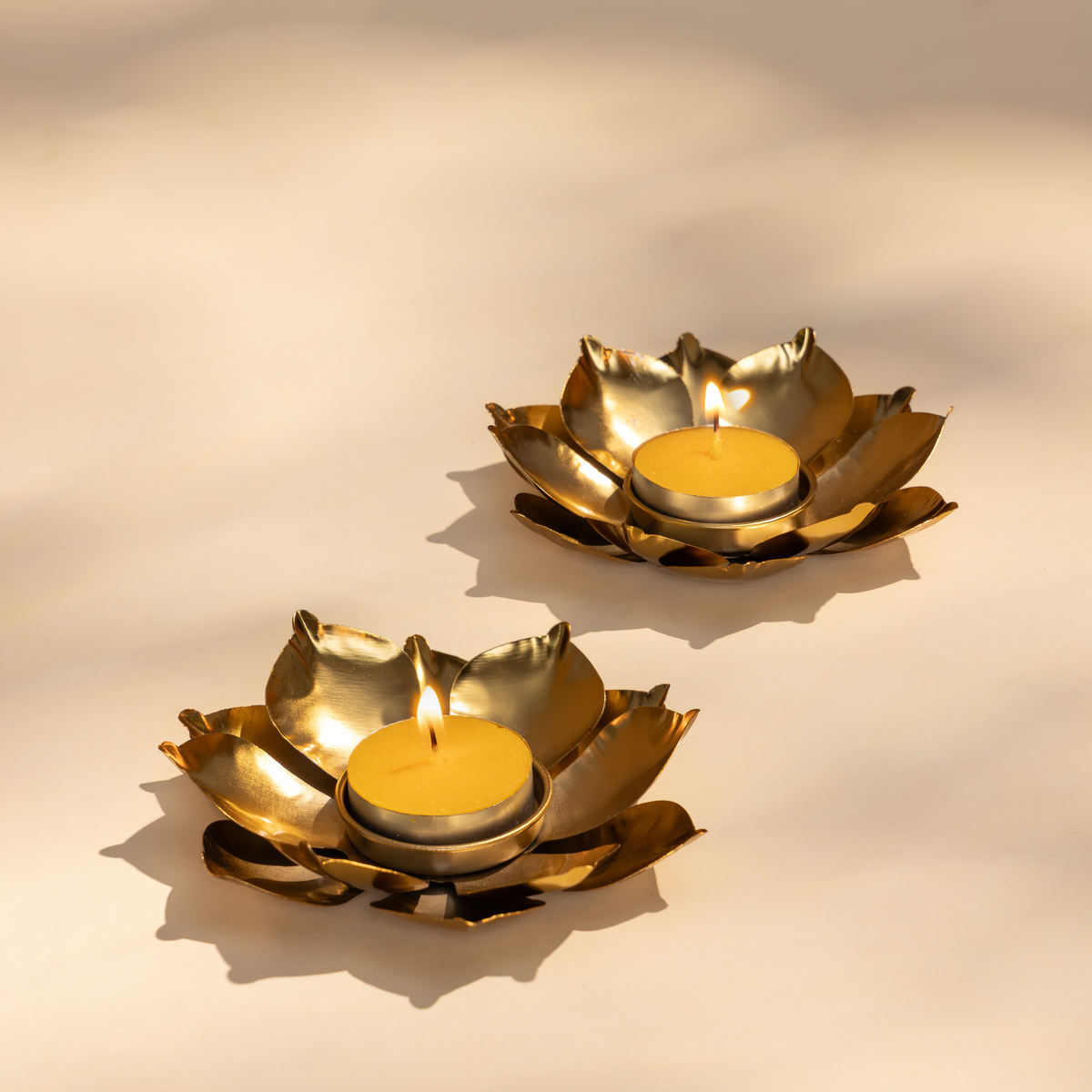 Two gold lotus-shaped candle holders for Diwali with lit candles
