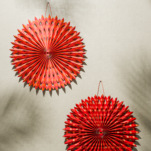 Two red decorative fans hanging for Diwali on a beige wall.