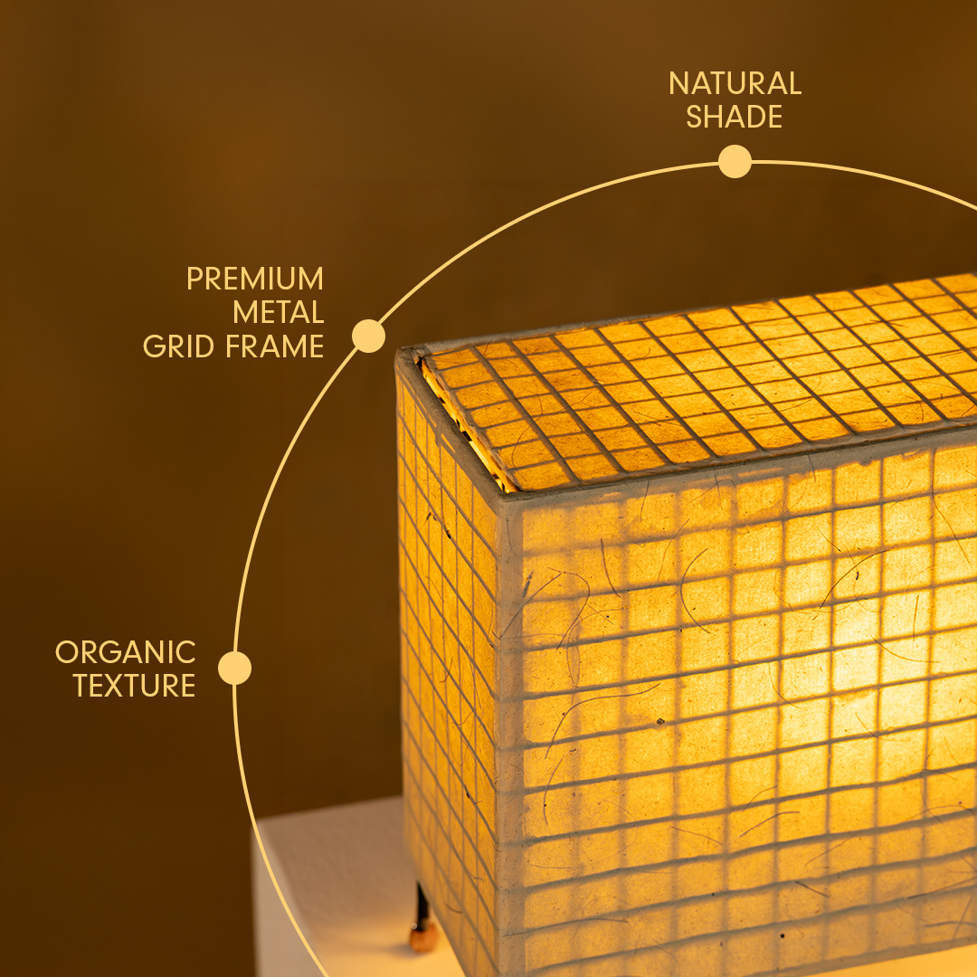 A close-up of a glowing square lamp shade made of a grid of small square panels, with a warm amber light. Text labels point to features: 'NATURAL SHADE,' 'PREMIUM METAL GRID FRAME,' and 'ORGANIC TEXTURE.